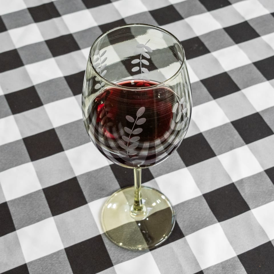 A glass of red wine with an etched leaf design sits on a black and white checkered tablecloth.