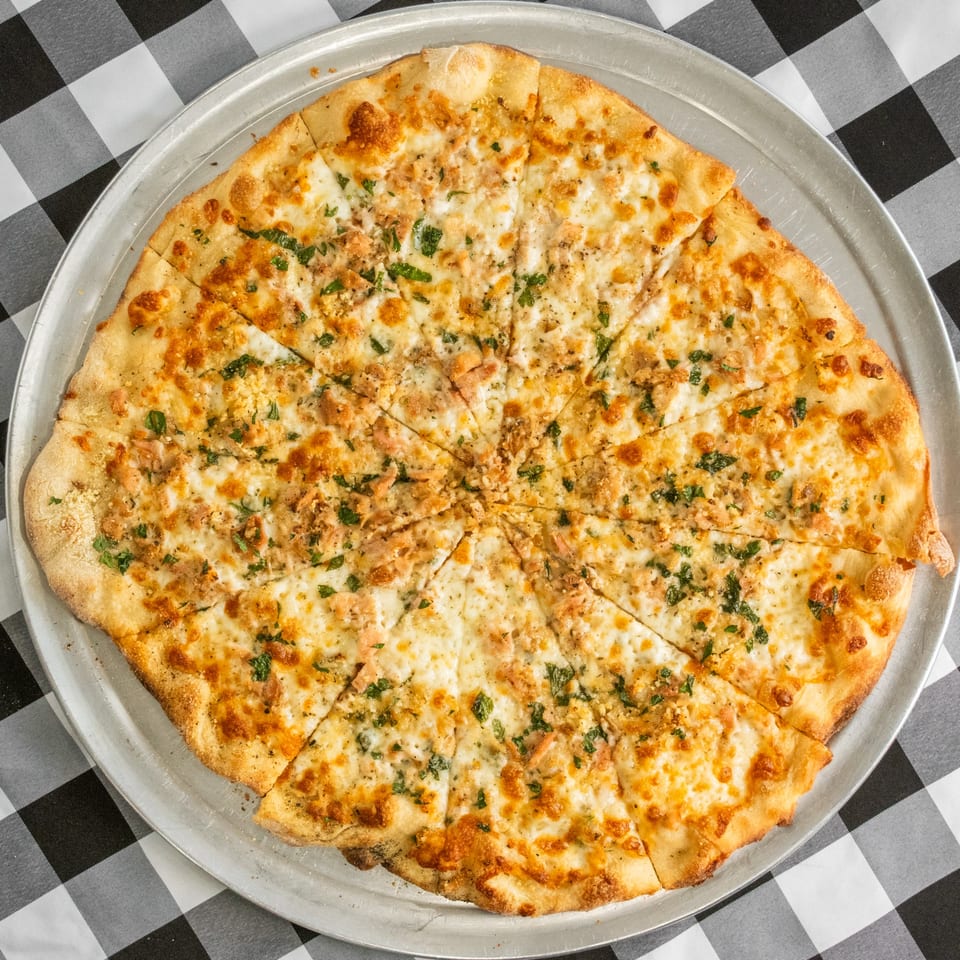 A white pizza with chicken and parsley, sliced into many pieces on a metal tray.