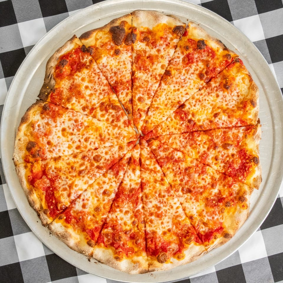 A freshly baked cheese pizza, sliced into many pieces, on a metal tray over a checkered tablecloth.