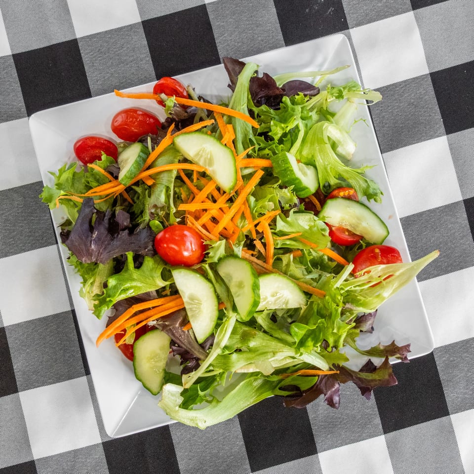 Fresh garden salad with mixed greens, cherry tomatoes, cucumbers, and shredded carrots on a white plate.