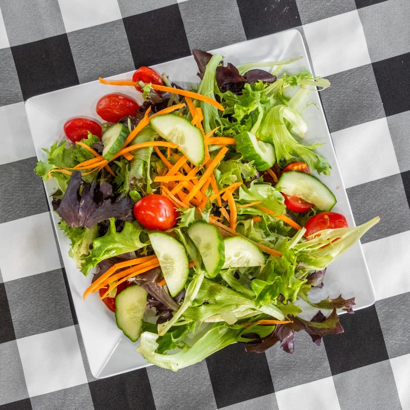 Fresh garden salad with mixed greens, cherry tomatoes, cucumbers, and shredded carrots on a white plate.