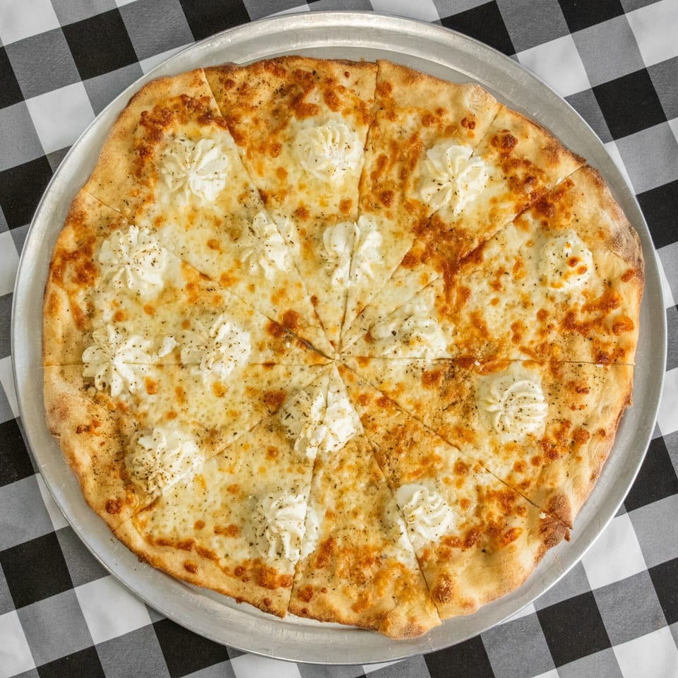 A white pizza with dollops of ricotta cheese and herbs, sliced on a metal pan.