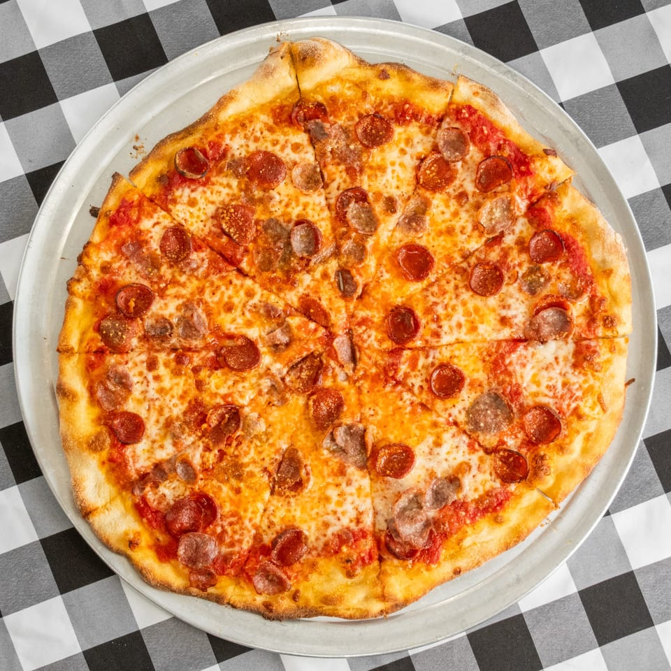 A freshly baked pizza with pepperoni and sausage, sliced into wedges on a metal pan.