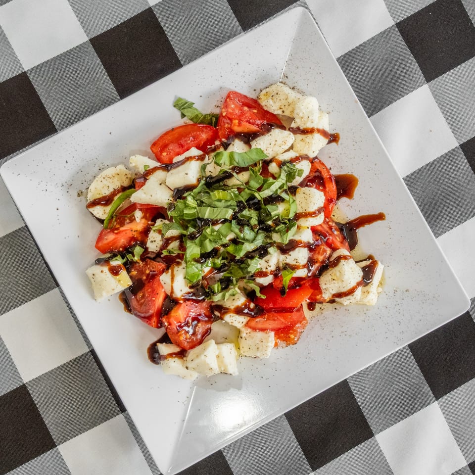 Caprese salad with fresh mozzarella, sliced tomatoes, basil, and balsamic glaze on a white plate.