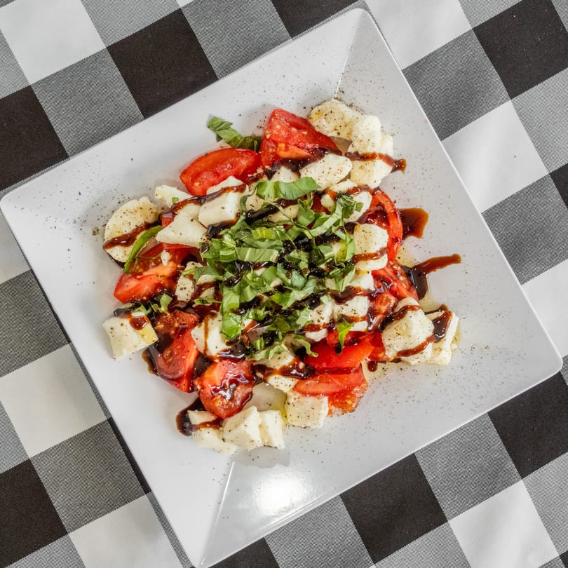 Caprese salad with fresh mozzarella, sliced tomatoes, basil, and balsamic glaze on a white plate.