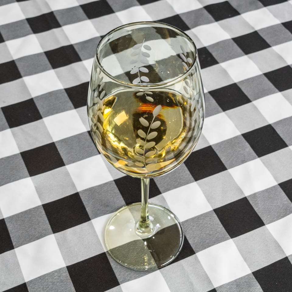 A wine glass filled with white wine sits on a black and white checkered tablecloth.