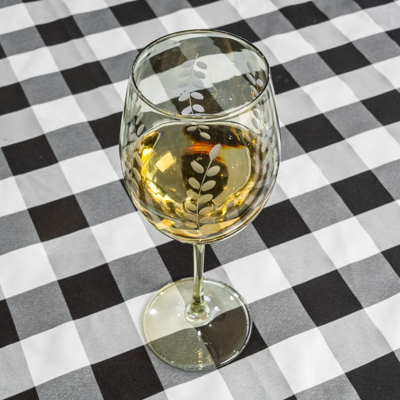 A wine glass filled with white wine sits on a black and white checkered tablecloth.