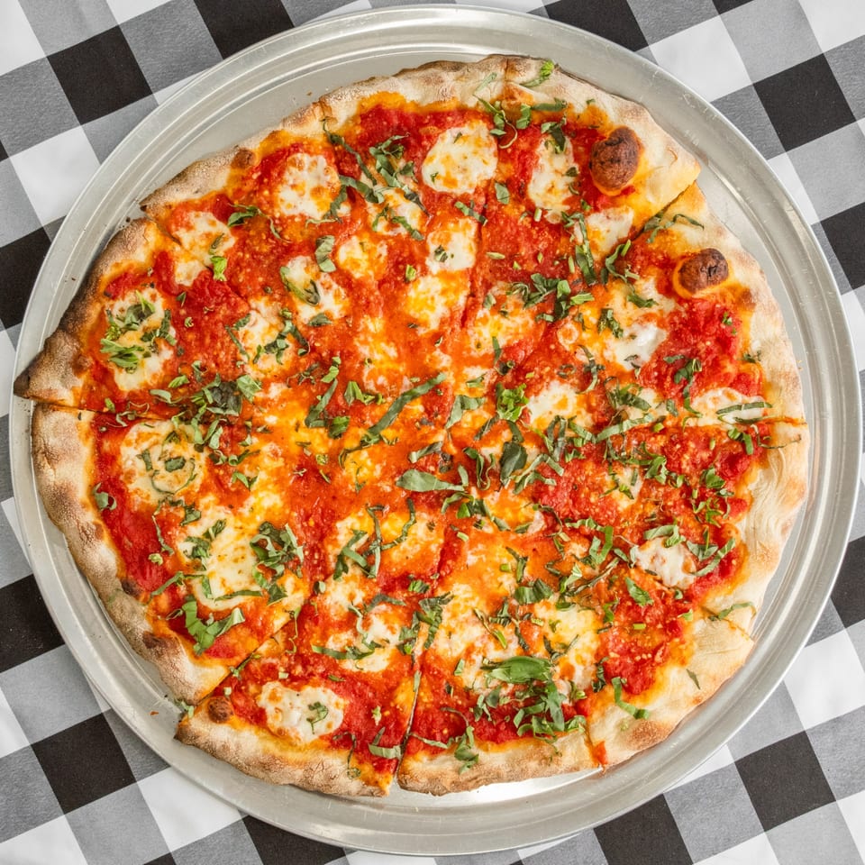A sliced Margherita pizza with fresh basil, mozzarella, and tomato sauce on a metal pan.